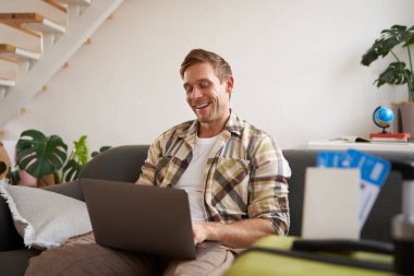 Laptoplu genç yakışıklı adamın portresi, pasaport ve iki uçak bileti hazırladı, bilgisayardaki yolculuğunu planladı, seyahat için oteller ve restoranlar ayarladı..