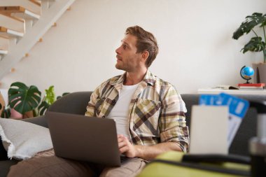 Laptoplu genç yakışıklı adamın portresi, pasaport ve iki uçak bileti hazırladı, bilgisayardaki yolculuğunu planladı, seyahat için oteller ve restoranlar ayarladı..
