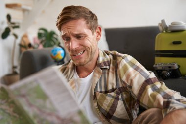 Elinde haritayla gülümseyen yakışıklı bir adam, bavulunu toplamış, tatile çıkıyor, tatile çıkmaya hazırlanıyor..