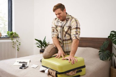 Genç bir adamın portresi, gezgin tatile çıkıyor, bavulunu ütülüyor, iç çamaşırlarını itmeye çalışıyor, bavullarını kapatıyor, tatil için bir sürü şey hazırlamaya çalışıyor. Turizm konsepti