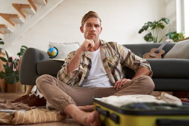 Stresli bir gencin bavulunu toplamasının portresi, tatilde ne giyeceğine karar vermesi, bavullara bakarken düşünmesi. Turizm konsepti