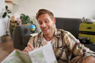 Elinde haritayla gülümseyen yakışıklı bir adam, bavulunu toplamış, tatile çıkıyor, tatile çıkmaya hazırlanıyor..