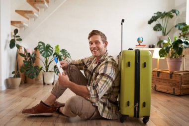 Yakışıklı genç bir adamın portresi, bavuluyla oturan bir turist, elinde pasaport ve uçak biletleri, tatile çıkıyor..