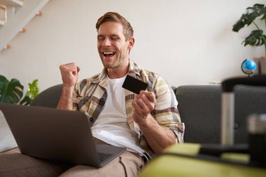 Mutlu adam portresi, gezgin, kredi kartı tutan ve dizüstü bilgisayar kullanan, tatil rezervasyonu yapan, yaz tatili için internetten bilet alan,.