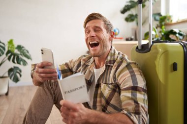 Bavullu, pasaportlu, akıllı telefon kullanan, tatile çıkan mutlu bir adam. İnsanlar ve seyahat kavramı