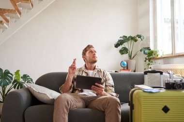 Turist portresi, iyi haberler için oturur ve bekler, dijital tablet tutar, bavul ve kamerayı tatil gezisi için hazırlar. Seyahat ve turizm konsepti