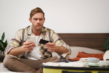 Bavuldaki mutlu adamın portresi, para transferi, internetten bilet alma, kredi kartı ve akıllı telefon uygulaması ile yatakta oturma, internet üzerinden ödeme..