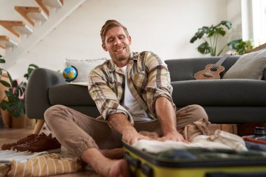 Genç bir adamın resmi, turist kıyafetleri bavulun içine sokmaya çalışıyor, tatil için hazırlanıyor. Turizm konsepti