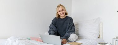 Yatağında ders çalışan genç bir kadının portresi, yatak odasında çalışıyor, dizüstü bilgisayarında ve defterlerinde Lotus pozu yazıyor, mutlu ve rahat görünüyor..