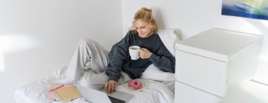 Genç bir kadının portresi, yatağında çalışan bir öğrenci, ödevlerini hazırlarken dinleniyor, çörek yiyor, laptopunu yatak odasında kullanıyor ve çay içiyor..