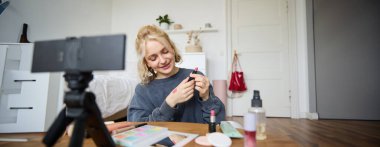 Güzel bir genç kadının portresi, sosyal medya yaratıcısı, dijital kameranın önünde oturan, makyajla ilgili video kaydeden, cildinde ruj örnekleri gösteren.