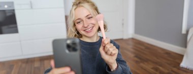 Genç bir kadının portresi, sosyal medya etkisinde, odasında selfie çekiyor, yerde oturuyor, akıllı telefon tutuyor ve fotoğraf için poz veriyor..