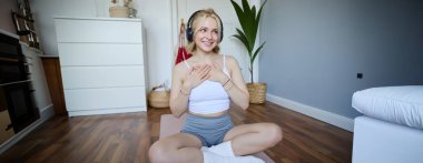 Spor yapan genç bir kadının evde kauçuk yoga minderi kullanması, müzik dinlemesi ve egzersiz yapması..