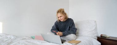 Yatağında ders çalışan genç bir kadının portresi, yatak odasında çalışıyor, dizüstü bilgisayarında ve defterlerinde Lotus pozu yazıyor, mutlu ve rahat görünüyor..