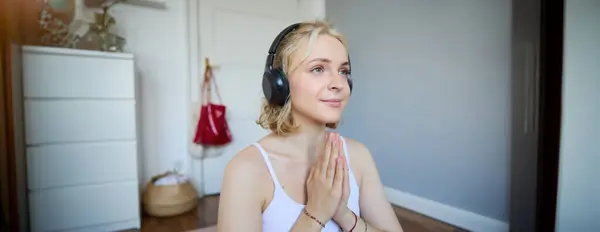 stock image Close up portrait of young relaxed woman in headphones, holding hands together in namaste gesture, listening to meditation podcast, practice yoga.