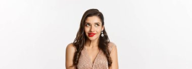 Elbise giymiş zarif ve güzel bir kadının yakın çekimi ve kırmızı ruj ile düşünme, sol üst köşeye bakma, baştan çıkarıcı dudak ısırma, beyaz arka plan üzerinde durmak.