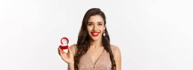 Güzel, esmer bir kadının nişan yüzüğünü gösteren, şık bir elbise giyen, evlilik teklifi alan, beyaz bir geçmişi olan yakın plan fotoğrafı..