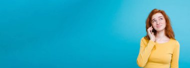 Yaşam tarzı kavramı - Kızıl kızıl saçlı kız arkadaşı ile cep telefonuyla konuşurken şok edici ve stresli ifade ile portresi. Pastel mavi arka plan üzerinde izole. Kopya alanı.