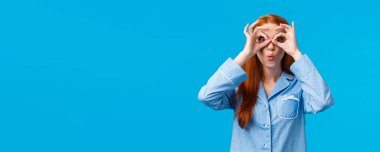 Kız diyor ki, vay canına kameraya bakıp özel tatil indirimi için harika bir fırsat yakalamış. Pijamalı çekici kızıl saçlı kadın parmaklarından ve kıvrılmış dudaklarından bakıp eğleniyor, mavi arka plan.