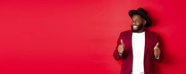 Neşeli siyahi adam partide eğleniyor, onay veriyor, gülümsüyor ve bir şeyden hoşlanıyor, kırmızı arka planda duruyor..