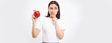 Asyalı bir kadının portresi, elinde kırmızı biber ve düşünme, düşünceli bir yüz, beyaz bir arka plan.