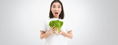 Şok olmuş bir kadın, çığlık atıyor, sebze tutuyor, çiğ yemek yiyor, diyette lahana yiyor, beyaz arka plan.