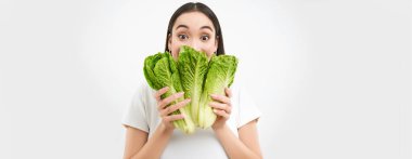 Hoş bir genç kadının portresi yüzünü lahana ile gösteriyor, sebzeleri seviyor, sağlıklı besleyici beslenme yemekleri yiyor, marul tutuyor, beyaz arka plan.