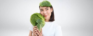 Güzel ve sağlıklı bir vejetaryen kadının portresi, elinde marul, kafasında lahana kabağı kabuğu, beyaz arka planı var..