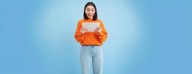 Gülümseyen Asyalı güzel bir kadın dijital tablette okuyor, cihaz videoları izliyor ya da video oyunları oynuyor, mavi arka planda duruyor..