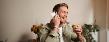 Genç yakışıklı adamın portresi telefonda konuşuyor, kahve içiyor ve gülüyor. Kafede oturan bir adam bir fincan kapuçino içerken hoş, hoş bir sohbet ediyor..