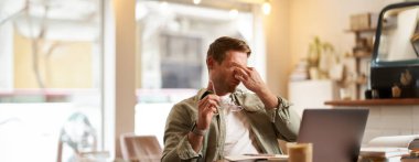 Dizüstü bilgisayara baktıktan sonra gözlerini ovuşturan yorgun bir adamın portresi. Bilgisayarda çalışıyor, kafede oturuyor, dinleniyor, gözlüklerini çıkarıyor..