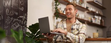 Kafedeki genç bir adamın görüntüsü, video görüşmesine bağlanıyor, çevrimiçi konuşuyor, arkadaşlarıyla sohbet ediyor ve gülümsüyor..