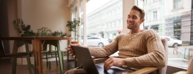 Çalışan genç bir profesyonelin portresi, laptopuyla kafede oturan, kahve içen ve internette çalışan, serbest çalışan bir adamın işini yapmak için çalışma alanını kullanması..