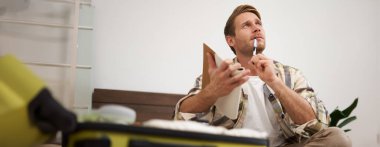 Bavul hazırlayan turistlerin portresi, listeyi gözden geçirmek, bavuluna koymak için eşyalar yazmak, deftere not almak, yatağa oturmak..