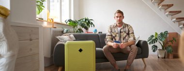 Yakışıklı bir gencin portresi, uçak biletleri, tatile gitmek, bavulla koltukta oturmak, havaalanına gitmek için taksi beklemek. Boşluğu kopyala