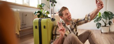 Elinde bavulla gülümseyen yakışıklı bir adamın portresi, bavulla selfie çekmesi, sosyal medyada tatile çıkmakla ilgili yazılar yazması. Turizm ve blog kavramı