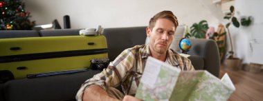 Yakışıklı genç adamın portresi, bavullu gezgin, kağıt haritaya bakıyor, tatilde nereye gideceğini seçiyor, tatile gidiyor, güzergahı seçiyor..