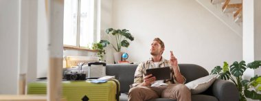 Turist portresi, iyi haberler için oturur ve bekler, dijital tablet tutar, bavul ve kamerayı tatil gezisi için hazırlar. Seyahat ve turizm konsepti