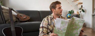 Genç bir adamın portresi, gezgin, bavulunu toplayan, seyahat haritasına bakan, tatil yerini seçen, tatilde güzergahı öğrenen. Turizm konsepti