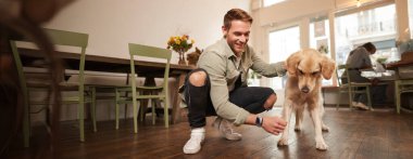 Evcil hayvan dostu kafede köpeğiyle vakit geçiren, Golden Retriever 'ı okşayan, eğlenen, ona ikramda bulunan mutlu adamın portresi..