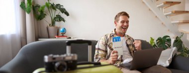 Laptoplu genç yakışıklı adamın portresi, pasaport ve iki uçak bileti hazırladı, bilgisayardaki yolculuğunu planladı, seyahat için oteller ve restoranlar ayarladı..