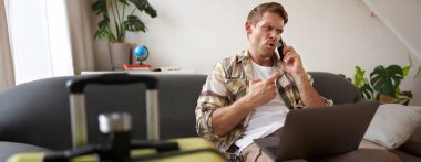 Telefonda tartışan öfkeli bir adamın portresi dizüstü bilgisayarı açık, bavulun yanında oturuyor, seyahat acentesine şikayet ediyor. Boşluğu kopyala