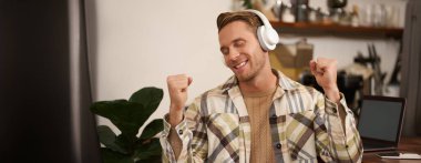 Yakışıklı mutlu adamın portresi, serbest çalışan ve kablosuz kulaklıkla müzik dinleyen, kafede sandalyesinde dans eden, kulaklıkla en sevdiği şarkıyı dinleyen..