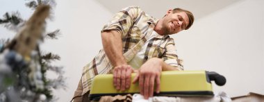 Genç bir adamın bavulu iterken, kapatmaya çalışırken yandan görünüşü bavulundan fırlamış, uzun bir tatile çıkıyor, tatile hazırlanıyor. Seyahat ve turizm konsepti