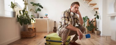 Üzgün ve yorgun bir adamın portresi, çantasında oturuyor, pasaportu ve uçak biletleri var, çok üzgün görünüyor..