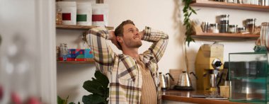 Mutlu yüzlü bir adam portresi, işini bitirdikten ya da projeyi bitirdikten sonra esneme, serbest çalışma, kafede kapalı dizüstü bilgisayarla oturmak, mutlu bir gülümseme..