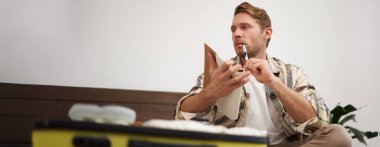 Genç bir adamın portresi, notlarına bakan bir turist, tatilde getireceği eşyaların listesi, bavulda giysiler, tatile gitmek. Turizm ve halk konsepti