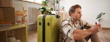 Genç bir adamın portresi, gezgin bavul ve cep telefonuyla oturur, akıllı telefondan sohbet eder..