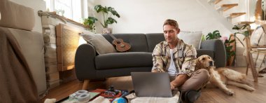 Köpekli bir adamın portresi, yerde oturuyor, bavul ve dizüstü bilgisayarı açık, internetten rezervasyon yaptırıyor veya alıyor, tatil planları yapıyor, tatile hazırlanıyor..