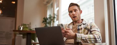 Telefonda korkunç haberler okuduktan sonra şok olmuş, endişeli bir yüz ifadesi. Kafede dizüstü bilgisayarla oturan yetişkin bir adam, akıllı telefondan smth okuduktan sonra endişeli tepki veriyor..